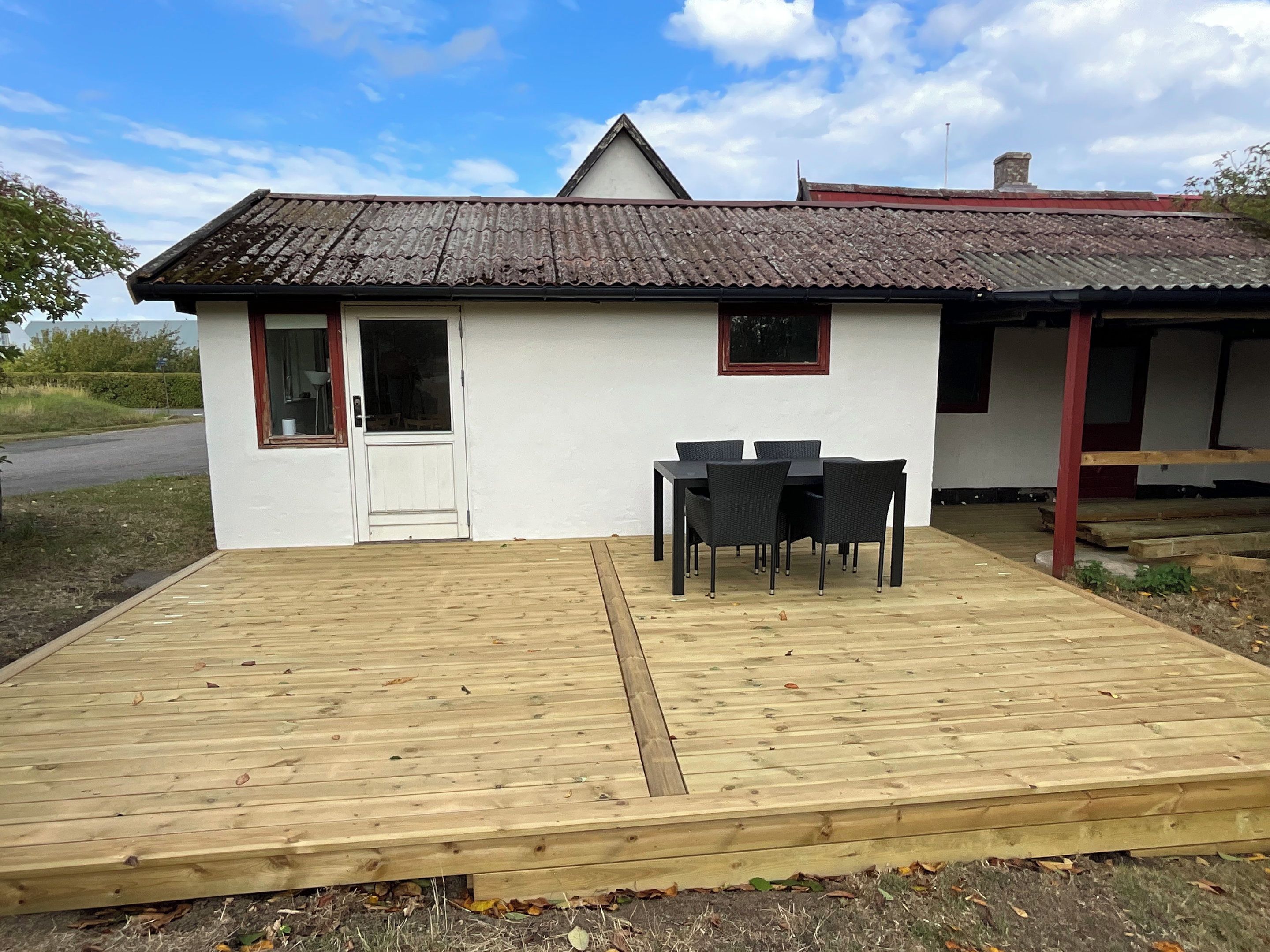 Ein kleines, weißes Gebäude mit einem Ziegeldach, einer Holzterrasse und einem Tisch mit Stühlen.