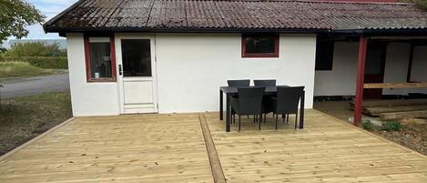 Ein kleines, weißes Gebäude mit einem Ziegeldach, einer Holzterrasse und einem Tisch mit Stühlen.
