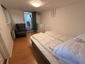 A bedroom with a bed, a chair, a wardrobe, and a door leading to a bathroom. - Lovely holiday home for peace and nature (Gudhjem)