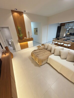 A modern living room with a sectional sofa, a dining area with a table and chairs, and a kitchen in the background.