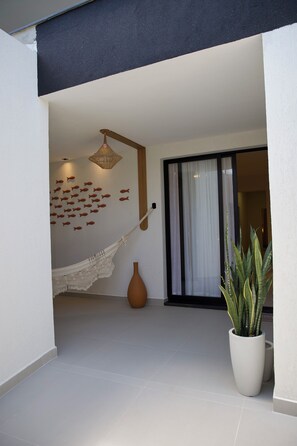 A modern interior space with a hammock, a decorative wall, a large potted plant, and a sliding glass door.