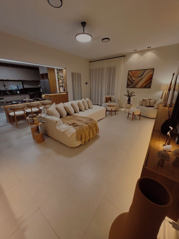 A modern living room with a sofa, chairs, a coffee table, and a dining area with a kitchen in the background.