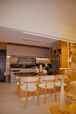 Cozinha moderna com ilha central, cadeiras de madeira e geladeira.