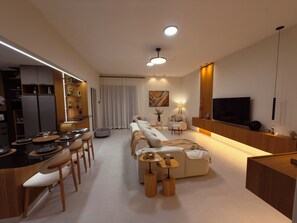 A modern living room with a sofa, dining area, kitchen, and a TV.