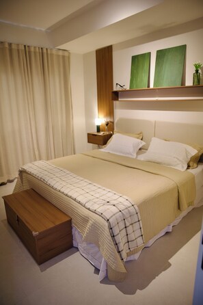 A hotel room with a bed, bedside table, lamp, and a small wooden bench.