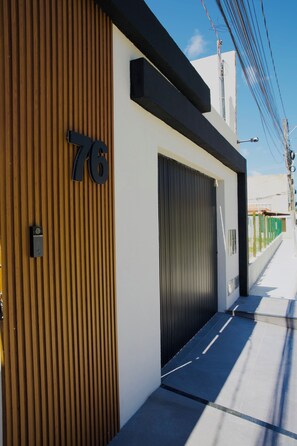 A modern building with a large garage door, a wooden panel facade, and a number '76' sign. - Casa Cazzoto, just steps from the Atalaia beachfront, the crab walkway, and the arches. (Aracaju)