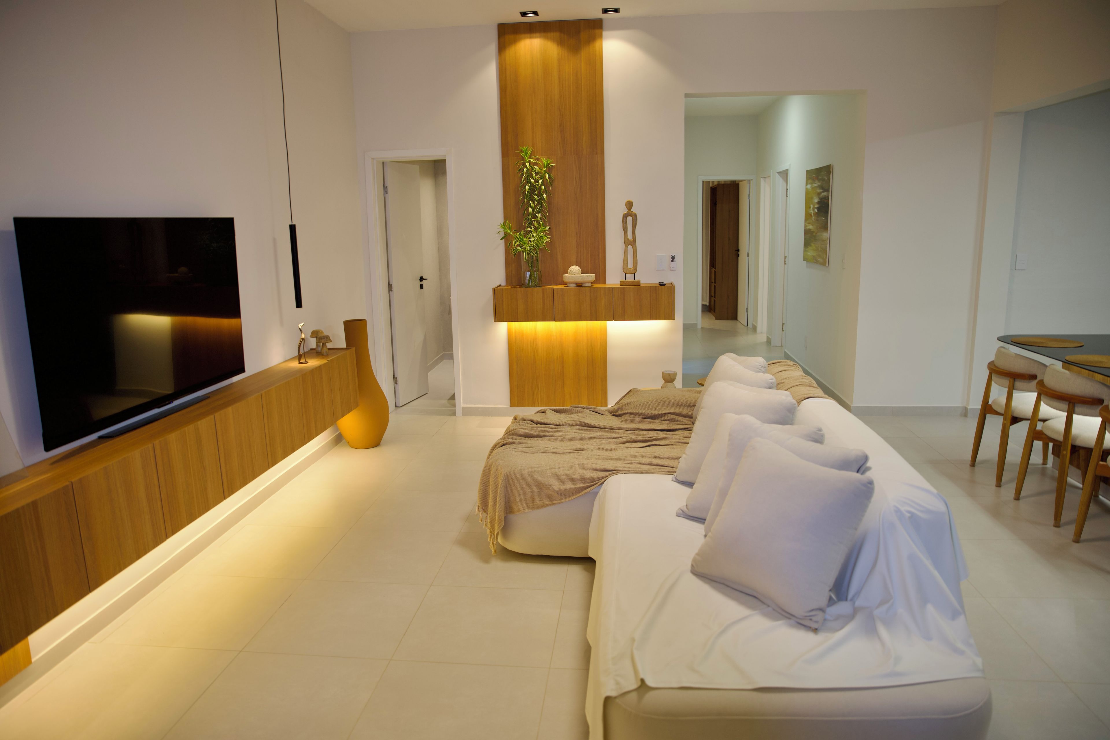 Une chambre d’hôtel moderne équipée d’un téléviseur à écran plat, d’une console en bois, d’un canapé, d’une table à manger et d’une plante.