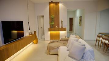 Une chambre d’hôtel moderne équipée d’un téléviseur à écran plat, d’une console en bois, d’un canapé, d’une table à manger et d’une plante.