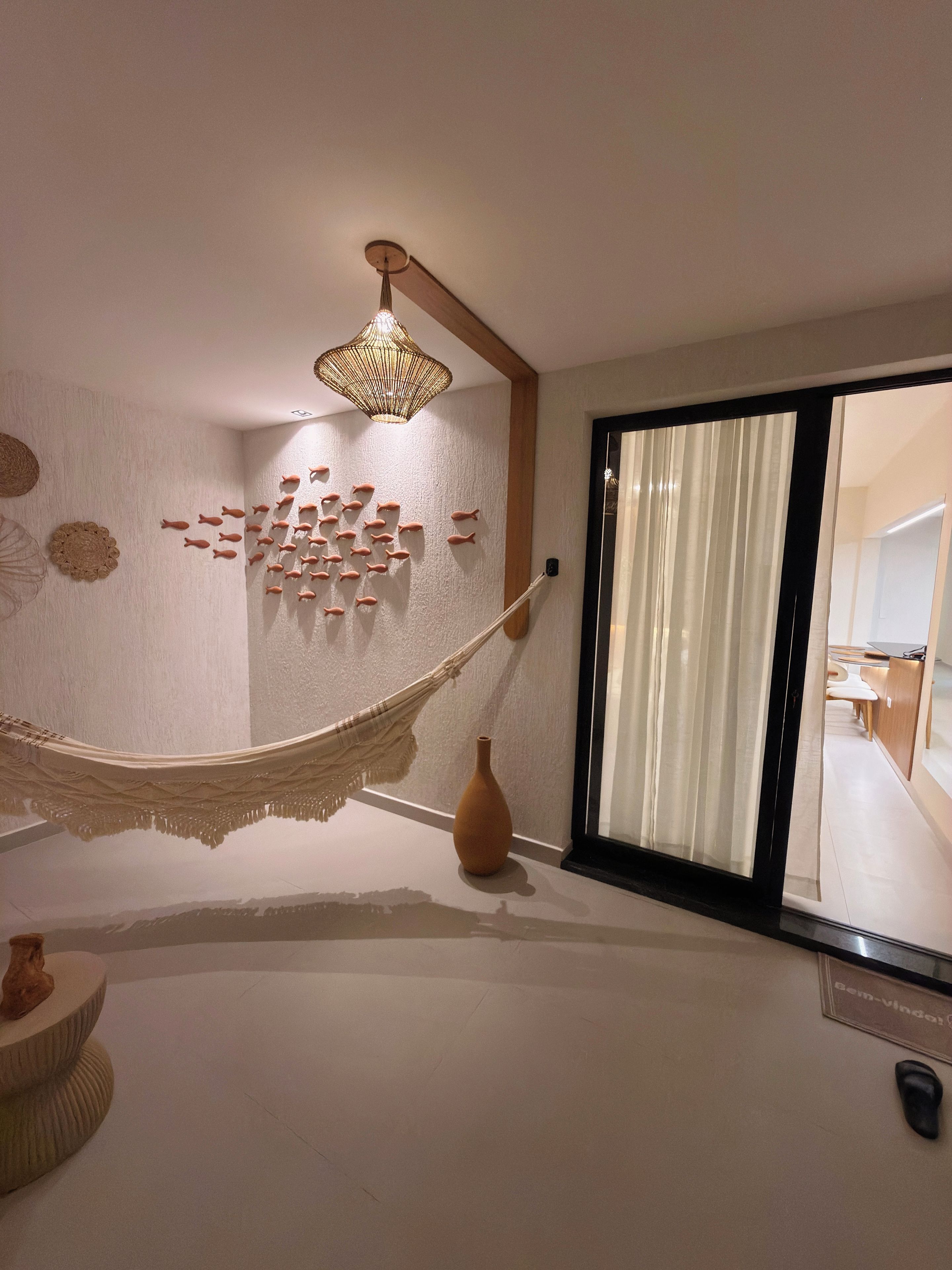 Une pièce avec un hamac, une décoration murale représentant des poissons, un luminaire suspendu et une porte-fenêtre coulissante.