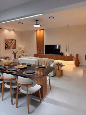 A modern living room with a dining area, a flat-screen TV, and a wooden cabinet.