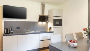 Eine moderne Küche mit integriertem Mikrowellenherd, Herd und Spüle. Ein Essbereich mit Tisch und Stühlen ist vorhanden, sowie eine Vase mit Blumen auf dem Tisch.
