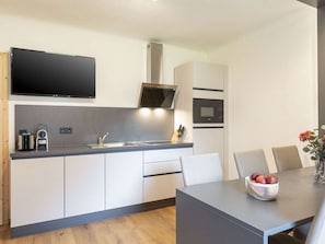 A modern kitchen with a built-in microwave, stove, and sink. There is a dining area with a table and chairs, and a vase with flowers on the table. - Apartment in Eisenerz With Balcony and Wi-fi (Eisenerz)