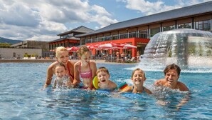 Ein Schwimmbecken mit darin befindlichen Personen, ein Gebäude mit roter Fassade und ein Wasserfall.
