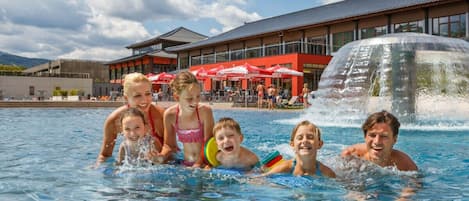 A swimming pool with people in it, a building with a red facade, and a waterfall feature.