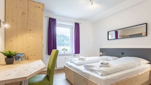 Ein Schlafzimmer mit einem Holzbett, einem Schreibtisch, einem Stuhl, einem Fenster mit Vorhängen und einem Spiegel an der Wand.