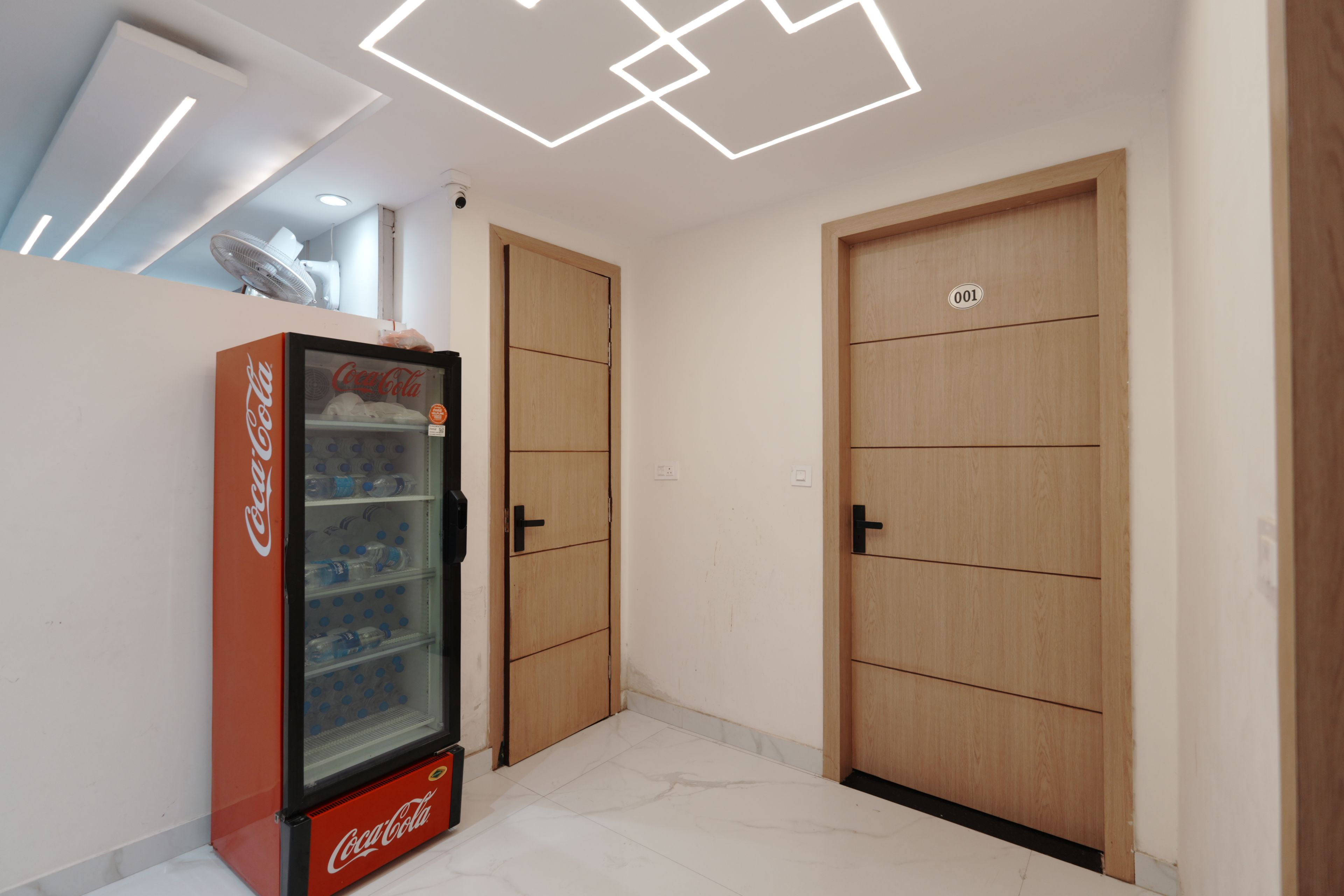 Una habitación con un refrigerador Coca-Cola, puertas de madera y un techo con lámparas geométricas.