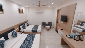 A hotel room with two beds, a small table, a chair, a TV, and a kitchenette area.