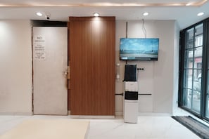 Un hall de hotel con una puerta de madera, un televisor montado en la pared y un dispensador de agua.