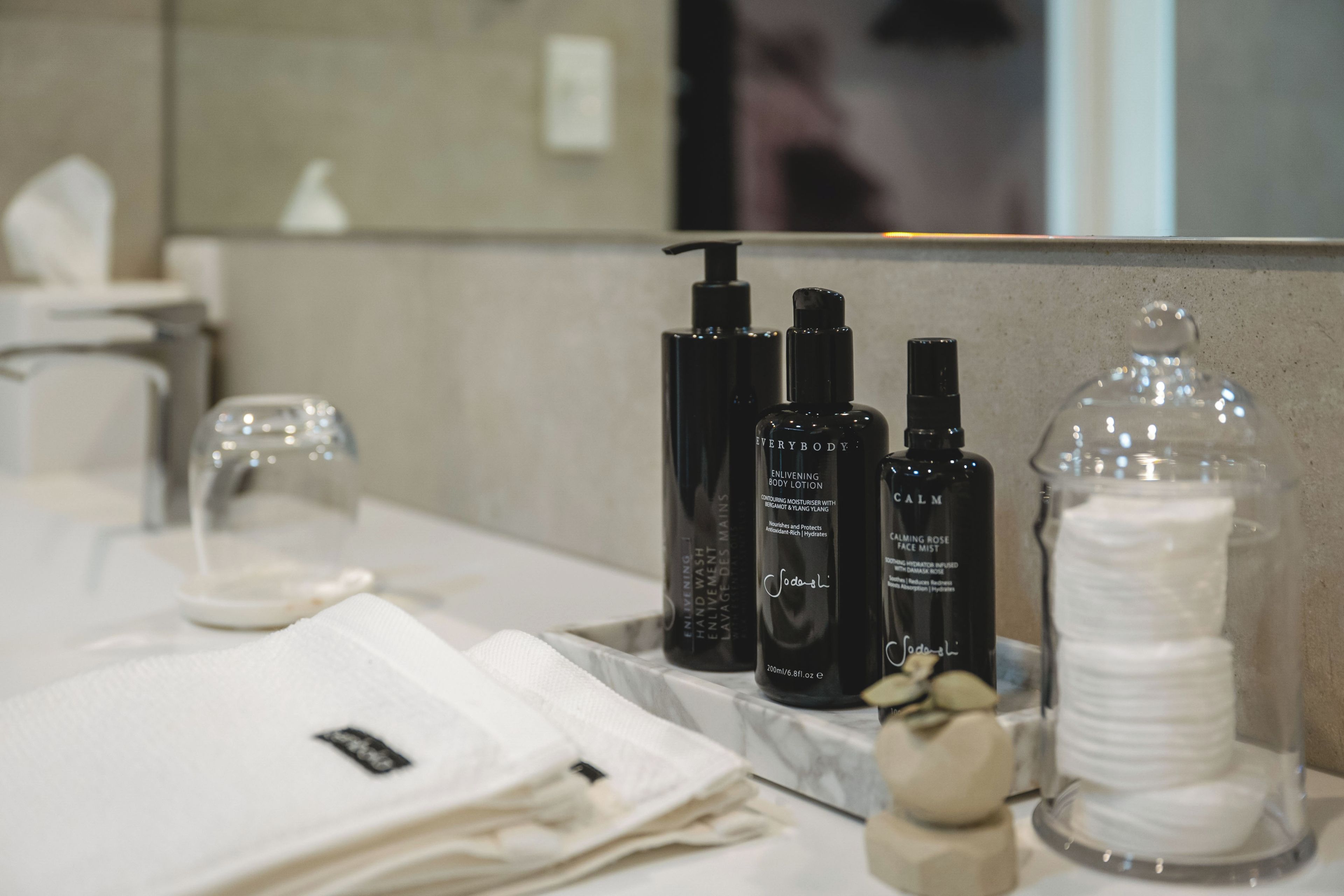 A bathroom vanity with toiletries and a glass container of cotton pads.