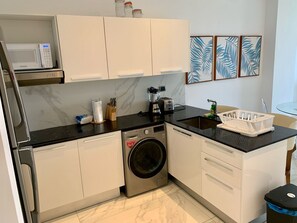 A compact kitchen with a built-in washing machine, a microwave, and a coffee maker. - Cana Rock Star Condo | Golf Course Views | Pool & Beach Club (Punta Cana)