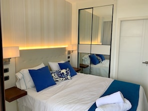 A hotel room with a bed, a nightstand, a mirror, and a door. - Cana Rock Star Condo | Golf Course Views | Pool & Beach Club (Punta Cana)