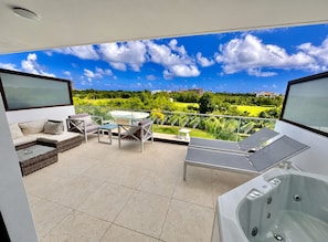 A balcony with a hot tub, seating area, and a view of a green landscape. - Cana Rock Star Condo | Golf Course Views | Pool & Beach Club (Punta Cana)