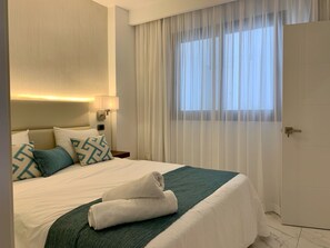 Une chambre d’hôtel avec un lit, une table de chevet, une lampe, une fenêtre avec des rideaux et une porte.