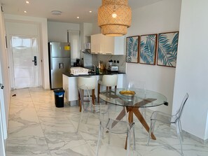 A modern kitchen with a glass dining table, clear chairs, and a hanging light fixture. - Cana Rock Star Condo | Golf Course Views | Pool & Beach Club (Punta Cana)