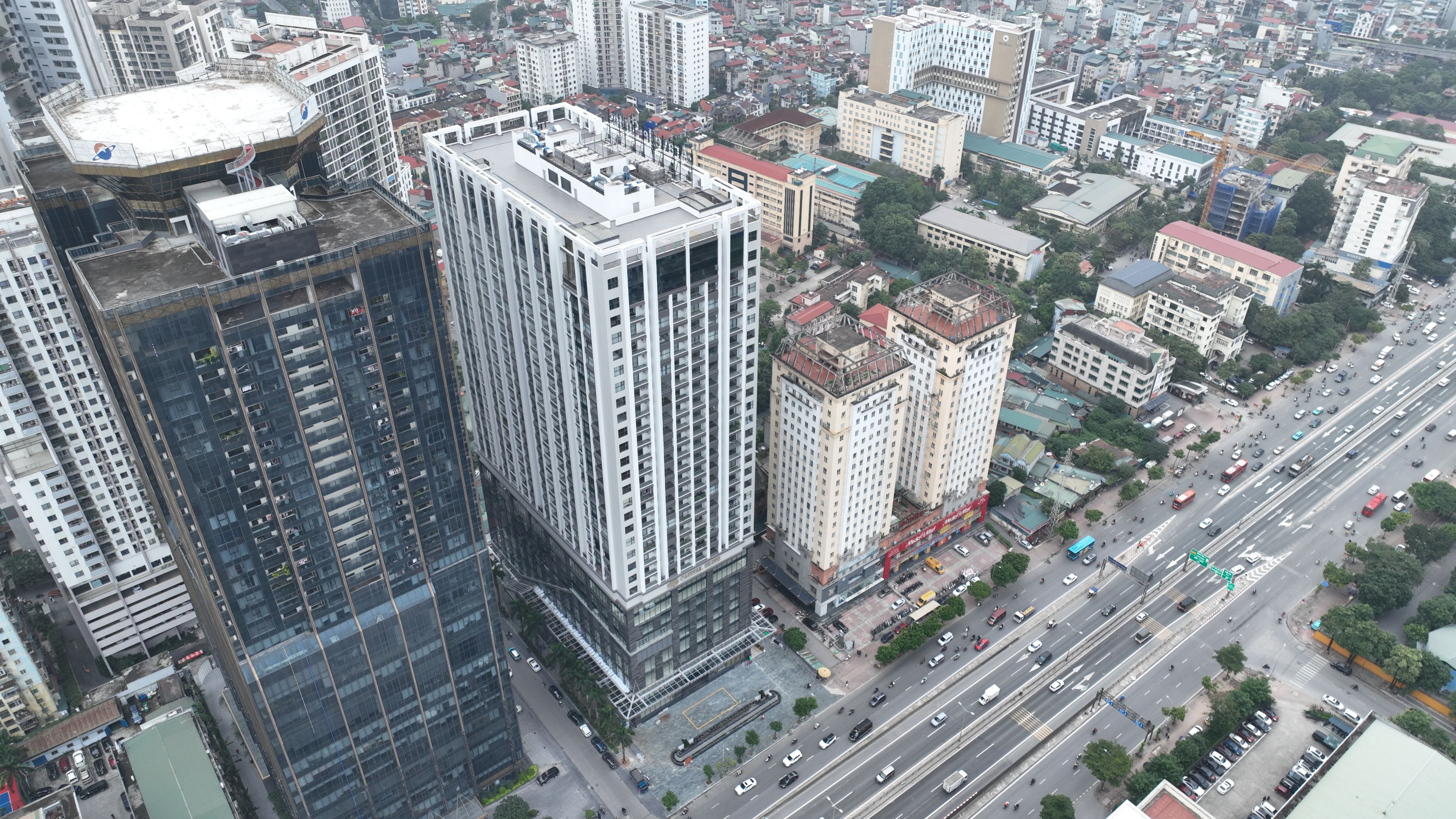 A high-rise building with multiple floors, surrounded by other buildings and a busy street with vehicles.