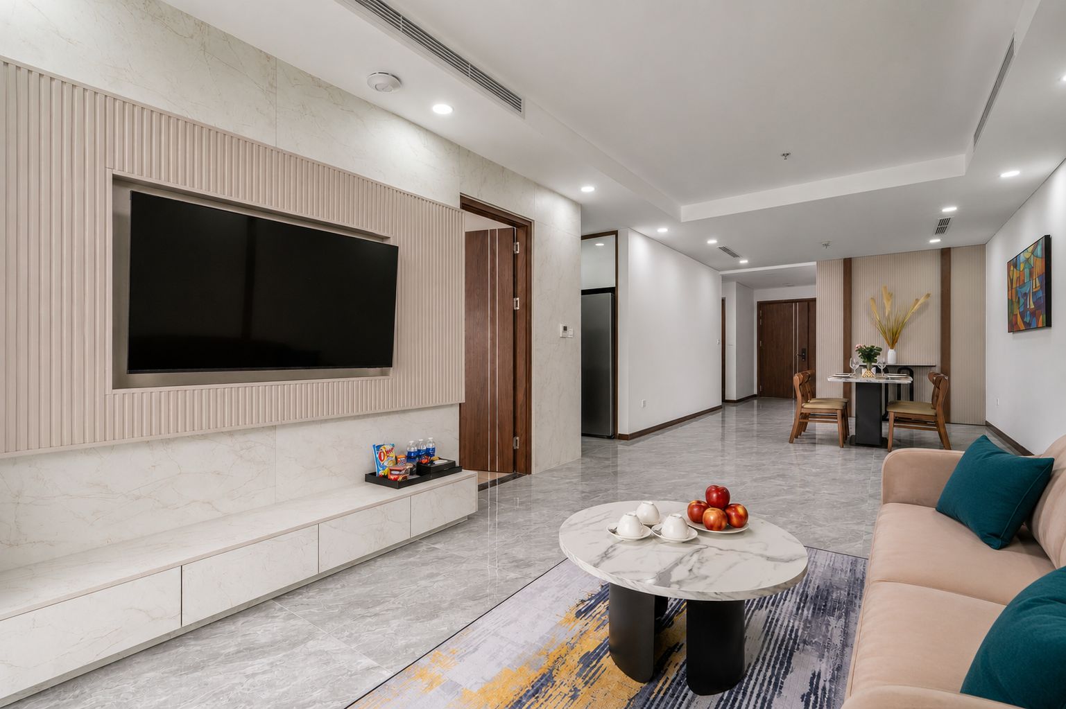 A modern living room with a large flat-screen TV, a marble coffee table, and a beige sofa.