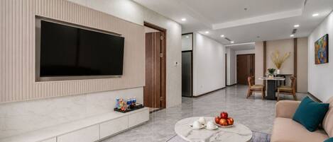 A modern living room with a large flat-screen TV, a marble coffee table, and a beige sofa.