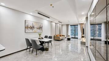 Una habitación de hotel moderna con zona de comedor, sofá y un amplio ventanal con cortinas.