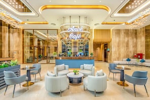 Een modern café met een centraal bedieningsgedeelte, een zithoek met banken en tafels, en een receptiebalie.