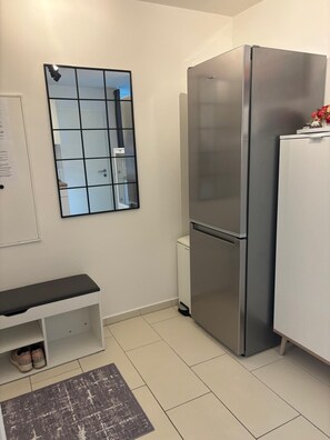 A compact kitchen with a stainless steel refrigerator, a white cabinet, and a small bench with shoes underneath. - Modern vacation apartment with panoramic views and a cozy, comfortable atmosphere (Oberteuringen)