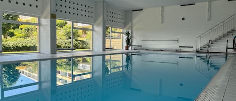 An indoor swimming pool with clear windows, a tiled floor, and a staircase leading to an upper level.