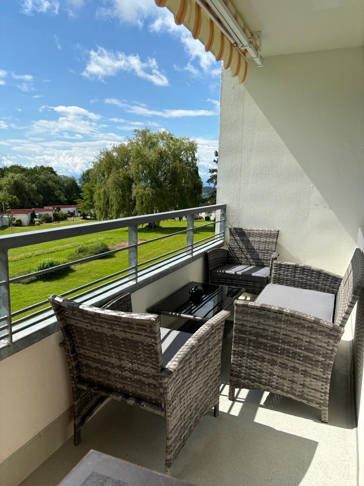 A balcony with wicker furniture, a small table, and a view of a green landscape.