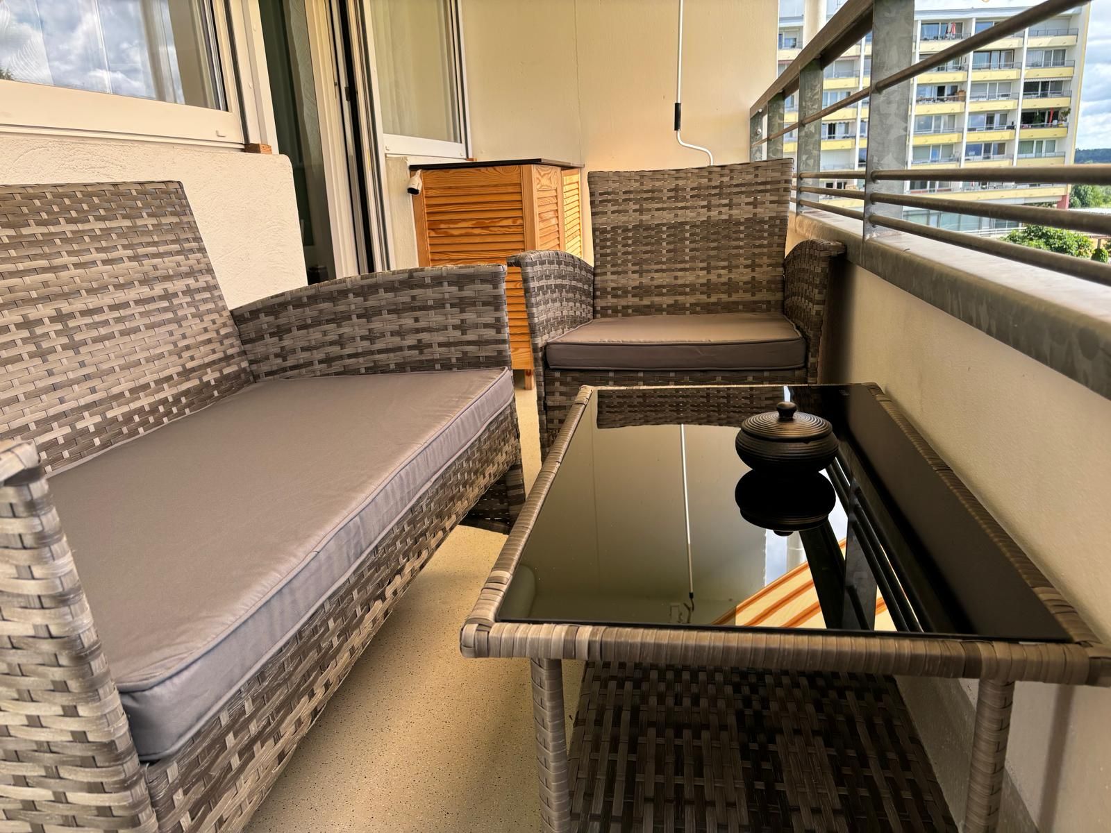 A balcony with wicker furniture, including a sofa and a table, and a view of a building in the background.