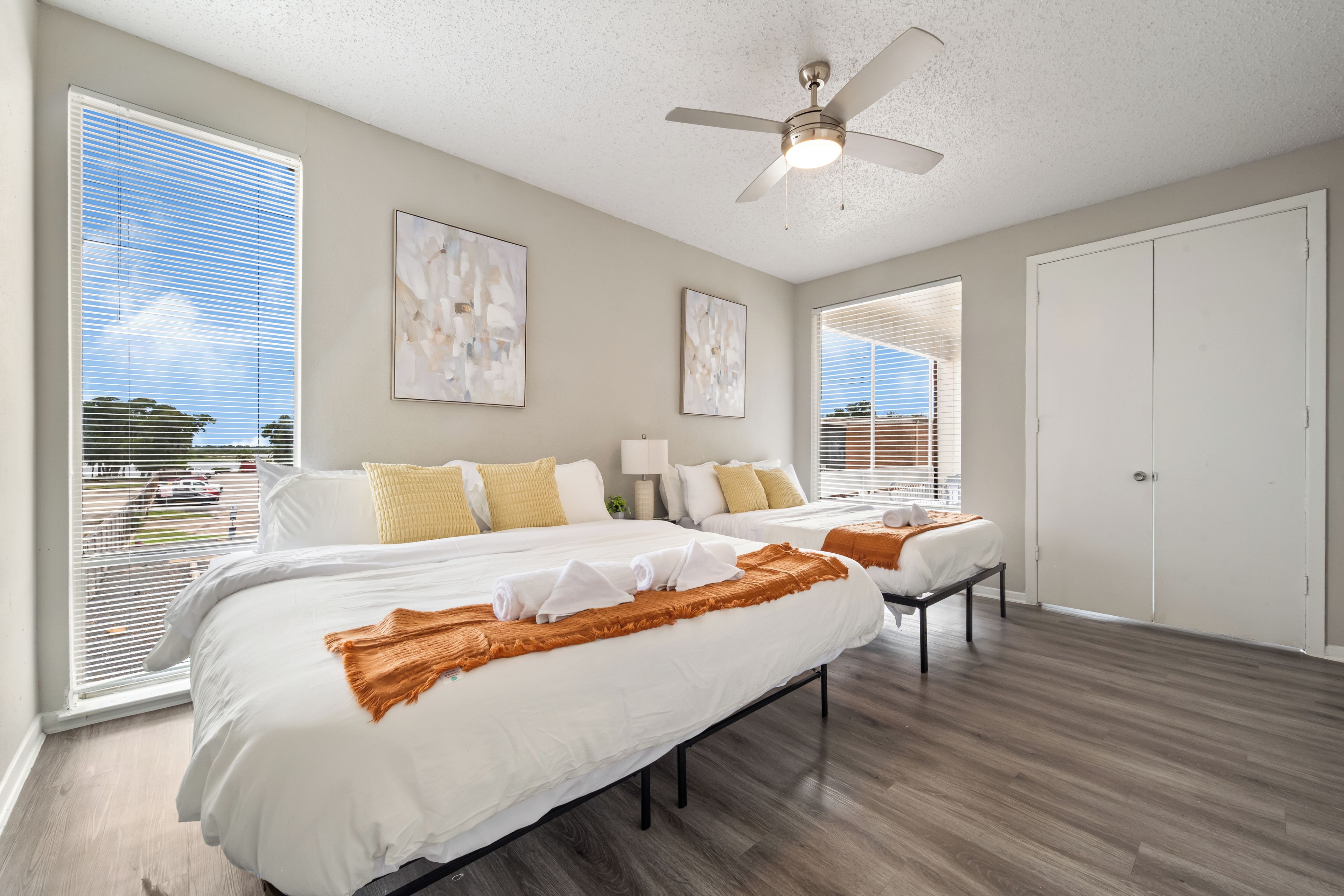 A hotel room with a large bed, two bedside tables, a ceiling fan, and large windows with blinds.