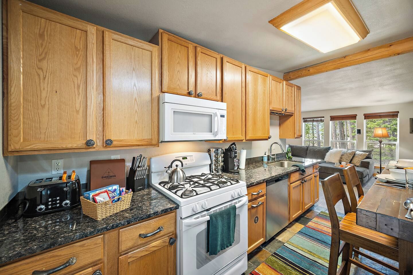A modern kitchen with wooden cabinets, a white microwave, a gas stove, and a dining area with a table and chairs.