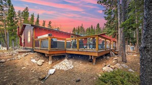 Eine Holzhütte mit einer Holzterrasse, umgeben von Bäumen, und einem klaren Himmel.