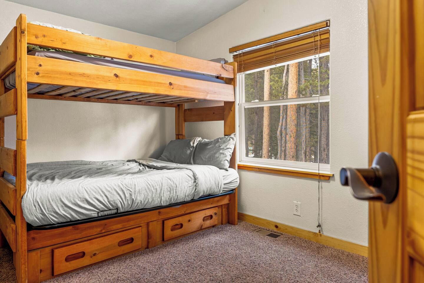 Una cama individual superpuesta con cajones de almacenamiento, una ventana con persianas y una puerta.