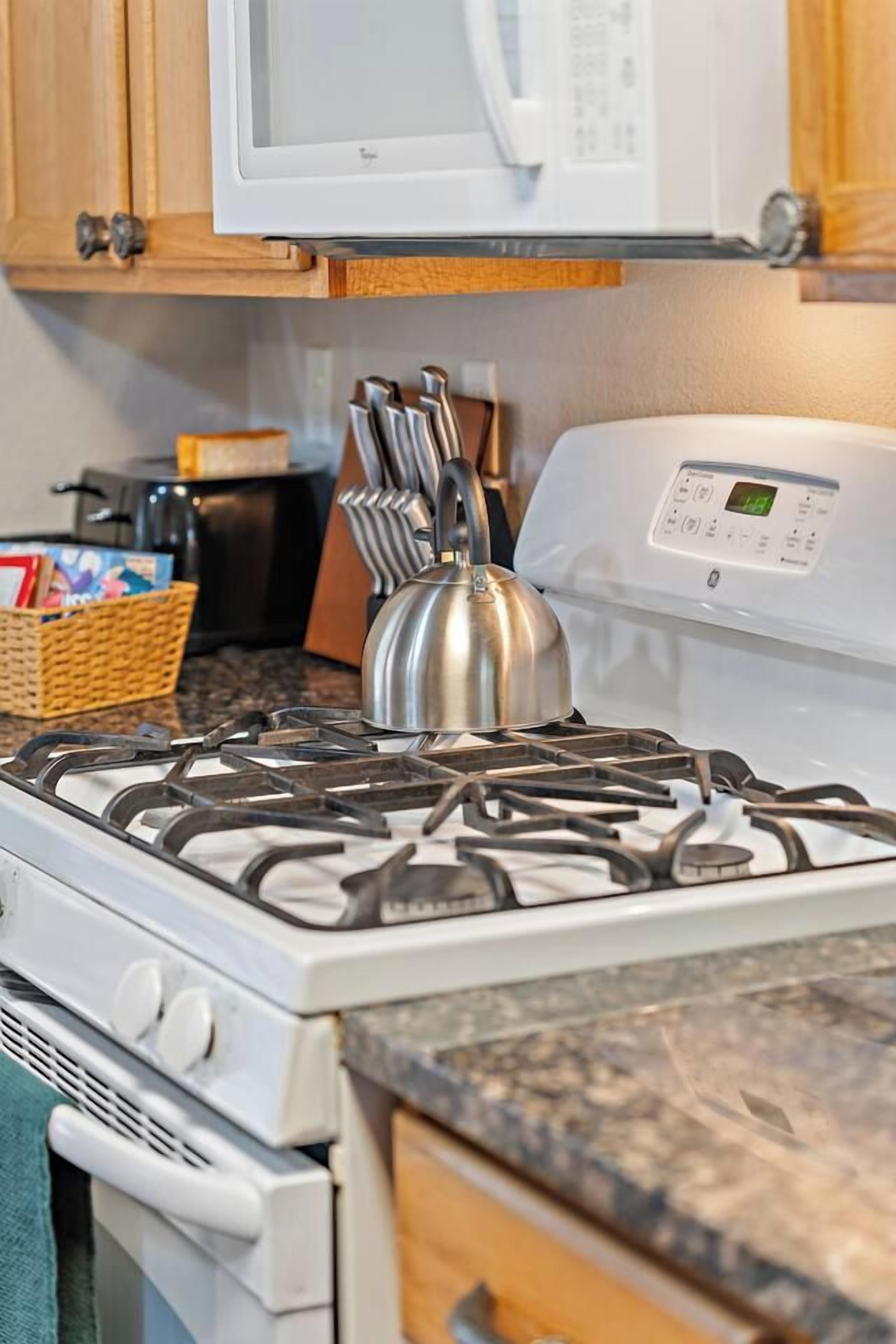 Una cocina con estufa a gas, horno, microondas y hervidor sobre la encimera.