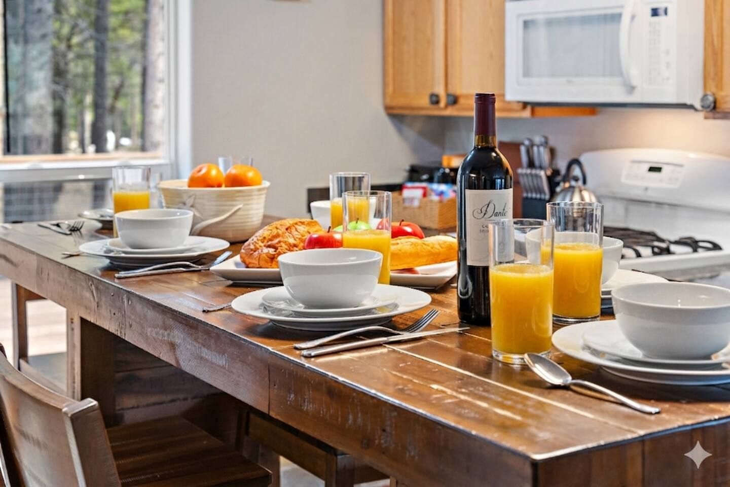 Desayuno con una mesa de madera, platos, tazones, croissants, jugo de naranja y una botella de vino.