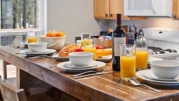 Una colazione con tavolo di legno, piatti, ciotole, croissant, succo d'arancia e una bottiglia di vino.
