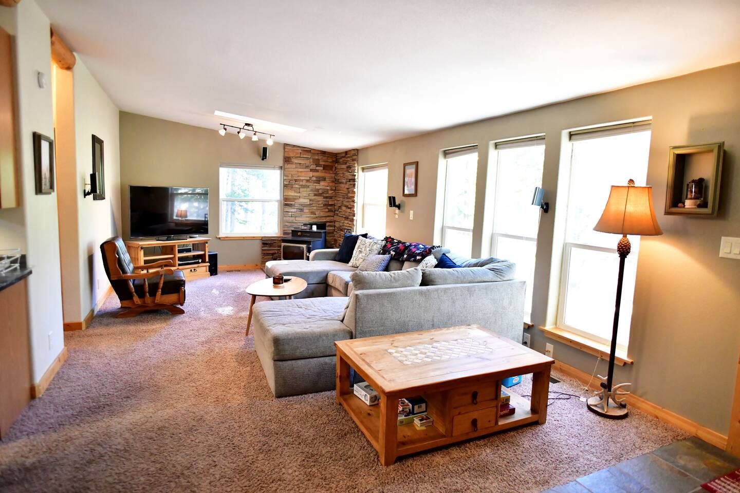 A living room with a stone accent wall, a flat-screen TV, a grey sofa set, a wooden coffee table, and a lamp.