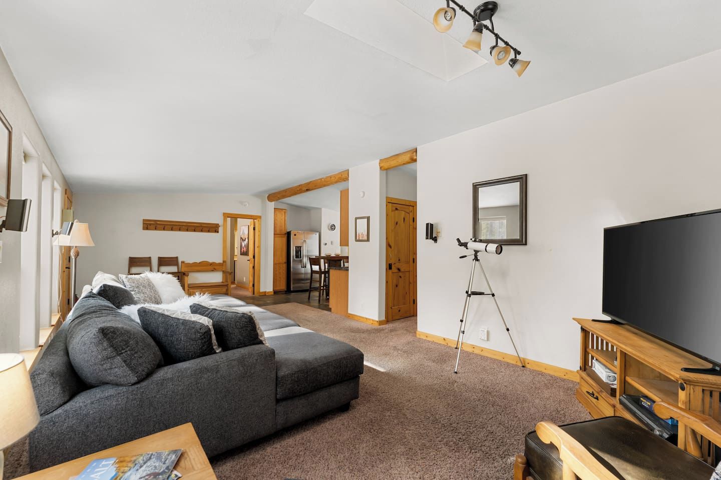 A modern living room with a sectional sofa, a TV on a wooden stand, and a telescope on a tripod.