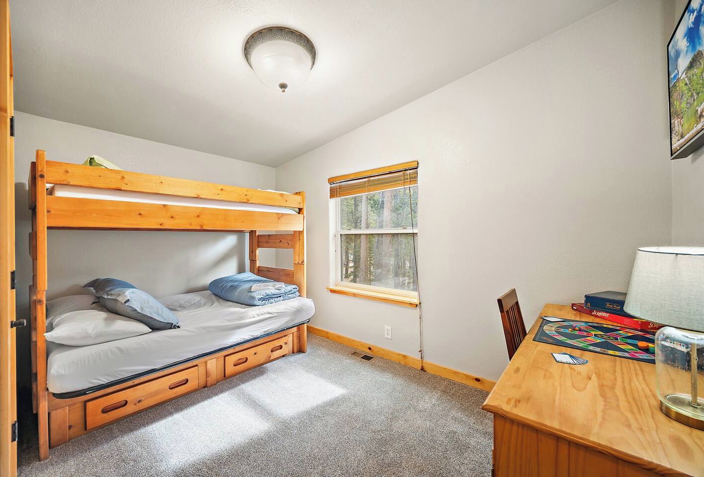 A bunk bed room with a window, a desk with a lamp, and a board game.