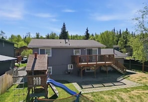 A two-story house with a deck, a slide, and a fenced yard.