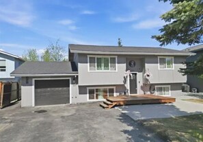 A two-story residential building with a garage, a front porch, and a small deck.