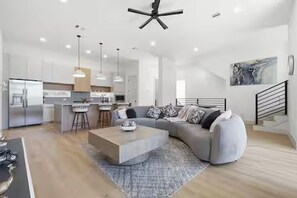 A modern living room with a sofa, coffee table, and kitchen area in the background. - Grand 3BR/3.5BA w/2-Car Garage mins to Downtown (Houston)